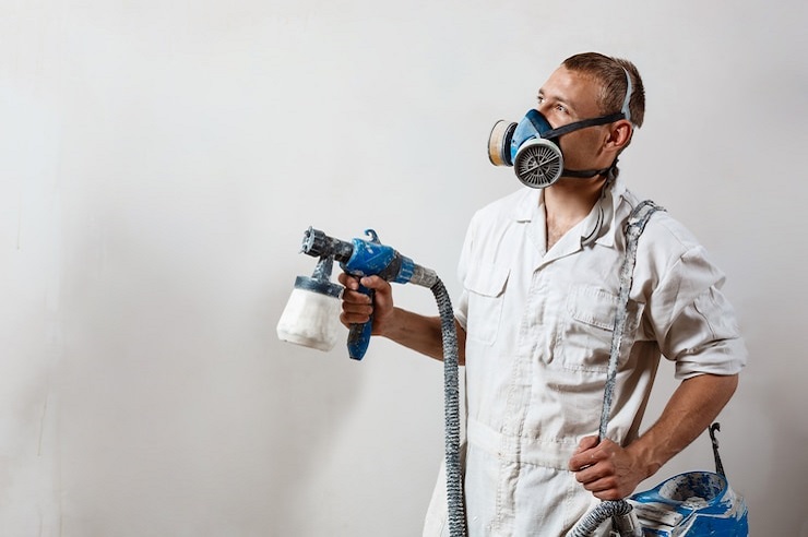 Worker painting wall with spray gun